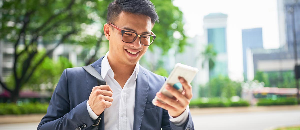 Man wearing glasses and grey blazer doing banking on his cell phone.